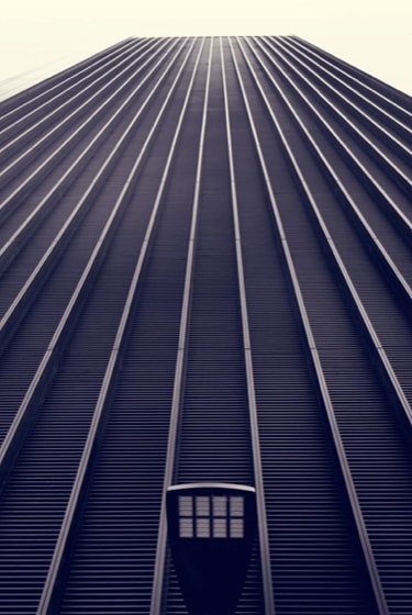 A low-angle view of a skyscraper with a repeating pattern of vertical lines, creating a sense of height and depth.