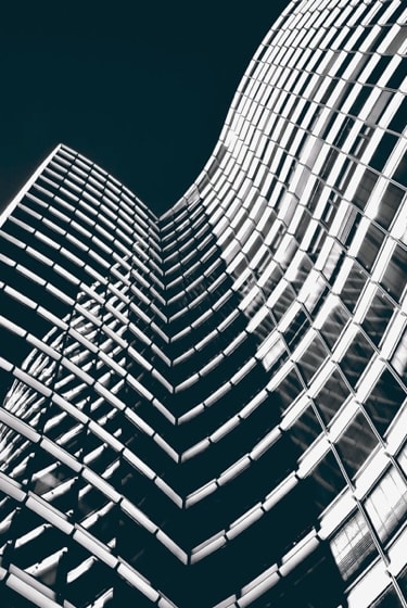 A dramatic low-angle view of a skyscraper with a curved, grid-like facade, illuminated against a dark sky.