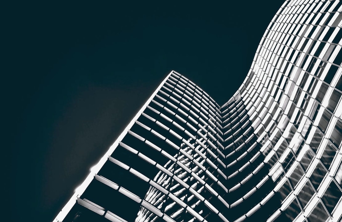 A dramatic low-angle view of a skyscraper with a curved, grid-like facade, illuminated against a dark sky.