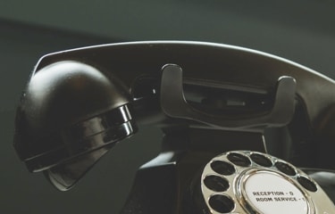 A vintage black rotary phone with a dial and buttons labeled 'Reception' and 'Room Service'.