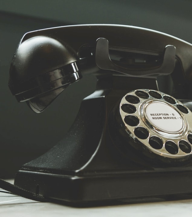 A vintage black rotary phone with a dial and buttons labeled 'Reception' and 'Room Service'.