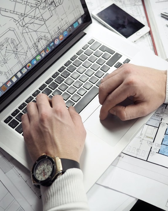 An architect working on a design project, using a laptop and blueprints.