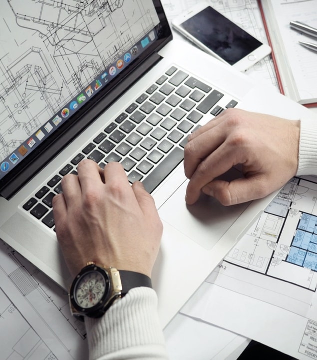 An architect working on a design project, using a laptop and blueprints.