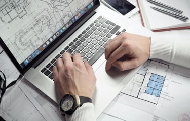 An architect working on a design project, using a laptop and blueprints.