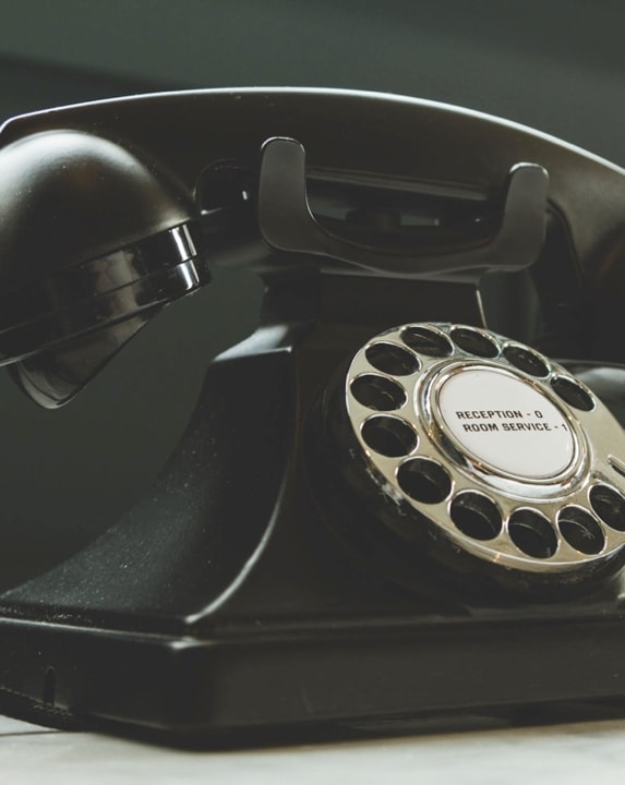 A vintage black rotary phone with a dial and buttons labeled 'Reception' and 'Room Service'.