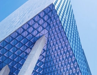 A modern skyscraper with a blue and white geometric pattern on its exterior, creating a sense of depth and dimension.