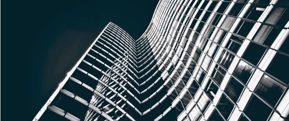 A dramatic low-angle view of a skyscraper with a curved, grid-like facade, illuminated against a dark sky.