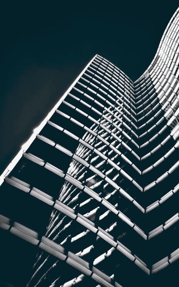 A dramatic low-angle view of a skyscraper with a curved, grid-like facade, illuminated against a dark sky.